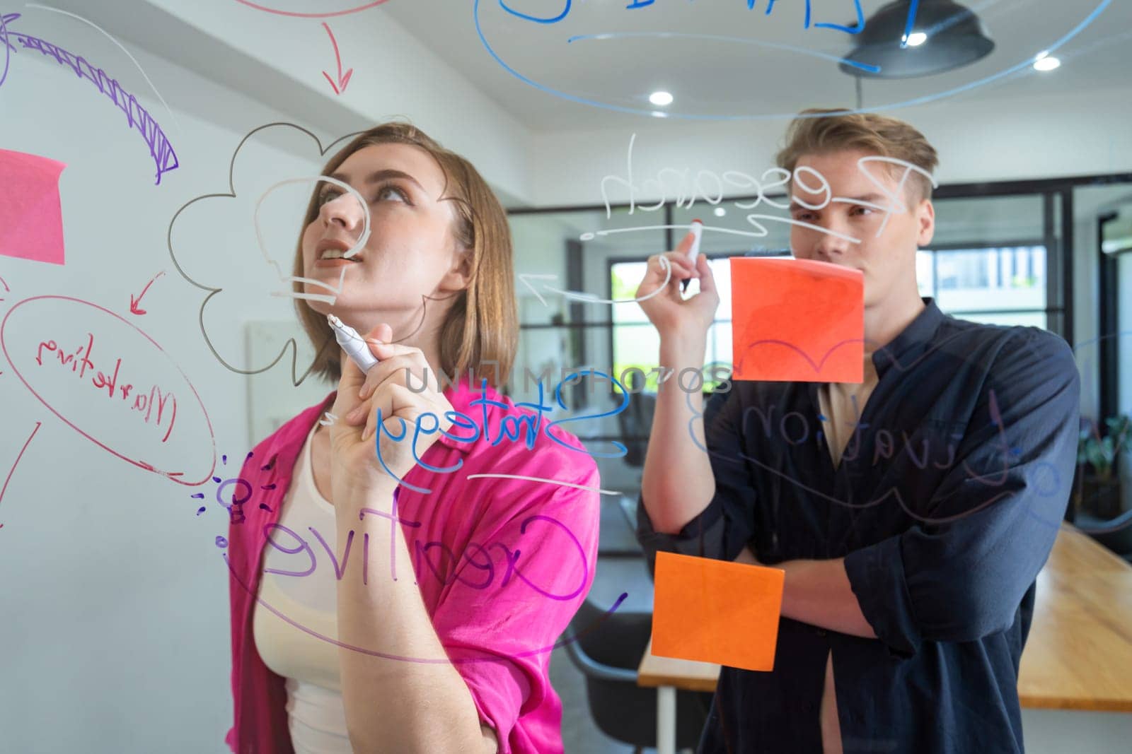 Couple of young creative start up business people brainstorming idea and solving problems by using sticky note and mind map at glass board, meeting room. discussing, working together. Immaculate.