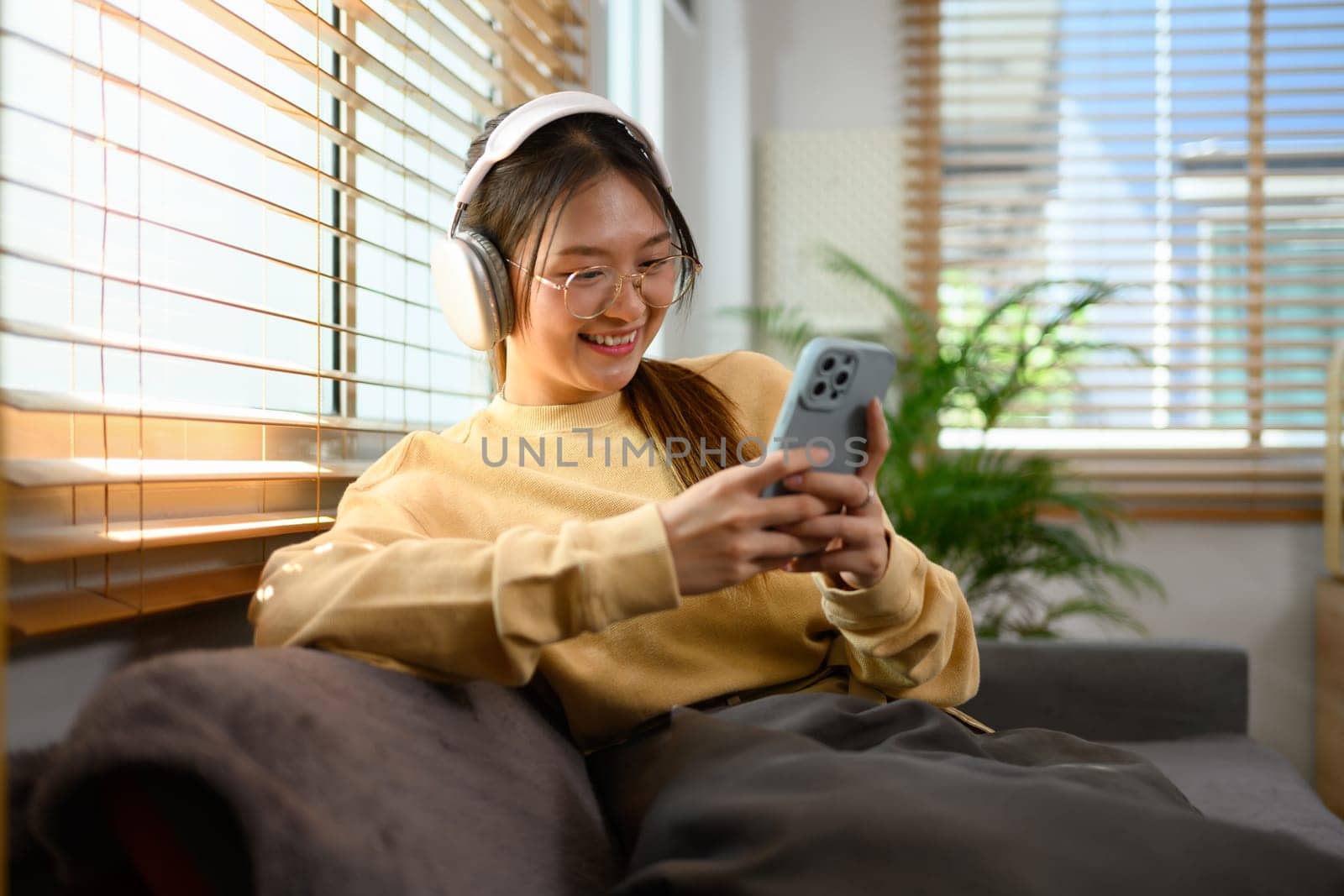 Cheerful young woman in headphone typing message on mobile phone.