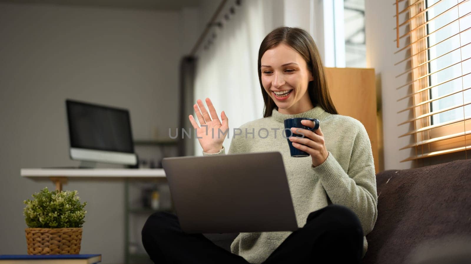 Cheerful young woman waving hand making video call on laptop at home.