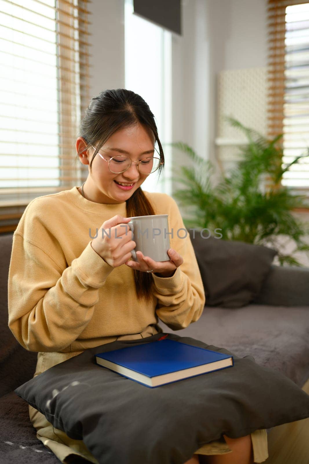 Young smiling woman drinking hot tea relaxing on couch at home.