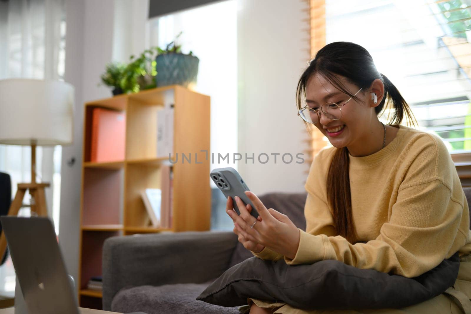 Young cheerful woman in eyeglasses typing message on mobile phone.