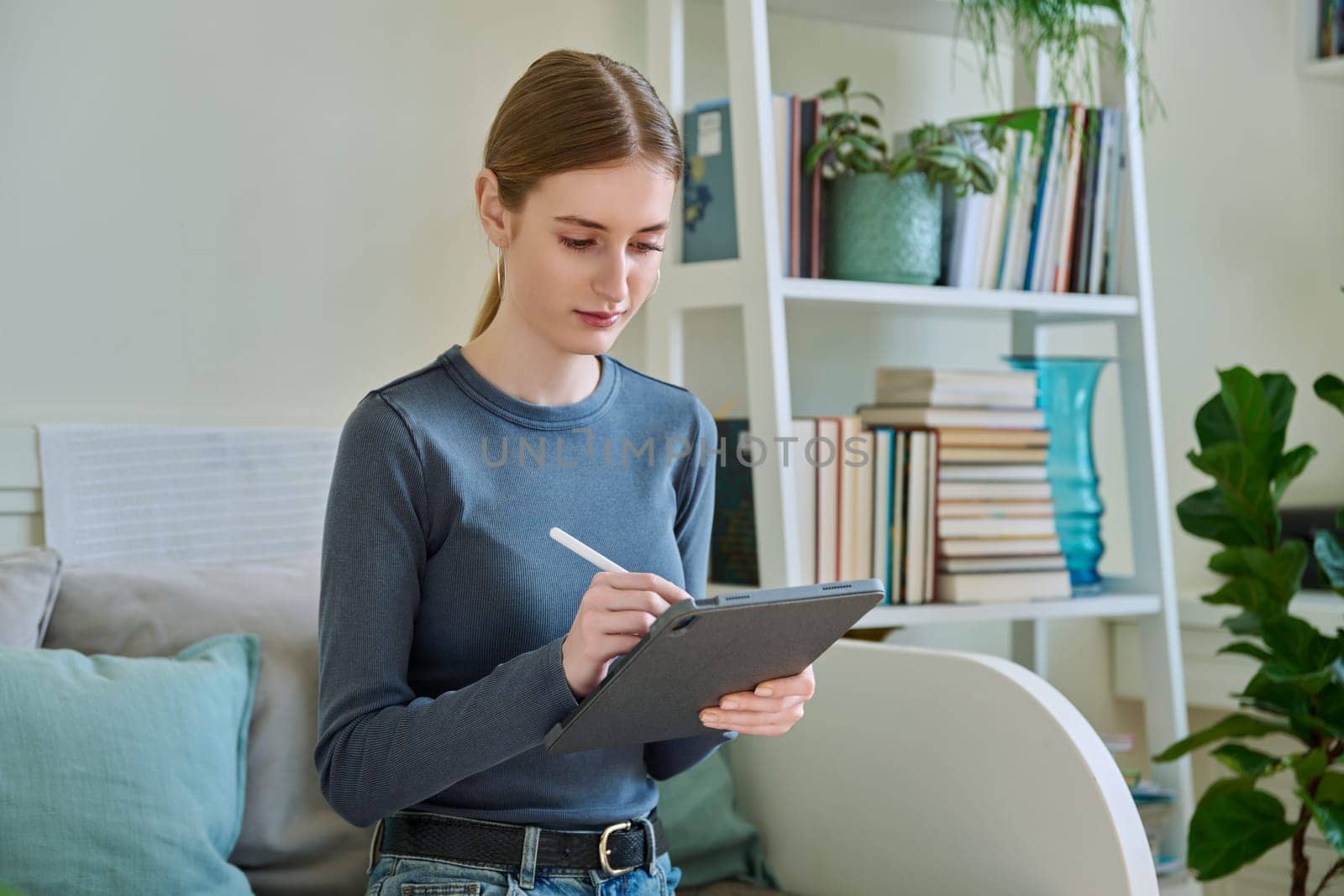 Young female teenager with digital tablet, stylus drawing illustrating sitting on couch at home. Technologies, leisure, creativity, education, freelance work, lifestyle, youth concept