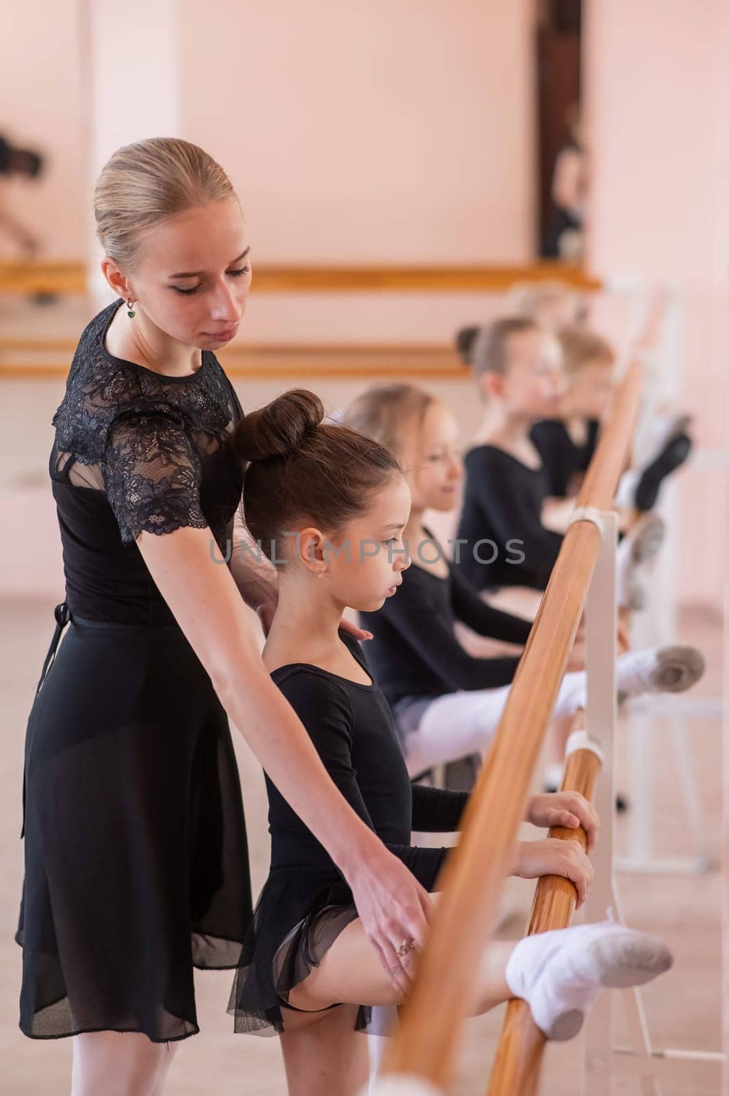 Caucasian woman teaches little girls ballet at the barre. Vertical photo. by mrwed54