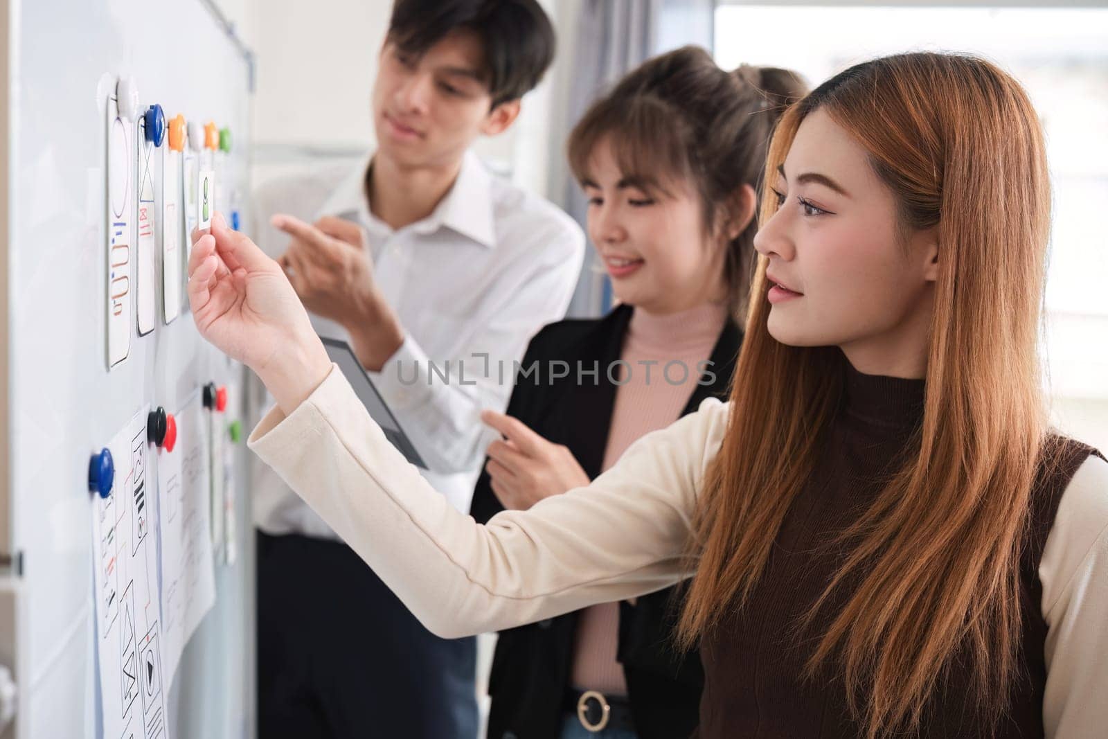 A team of software developers brainstormed to design a smartphone application by planning on a whiteboard and using it to develop the application system. by wichayada