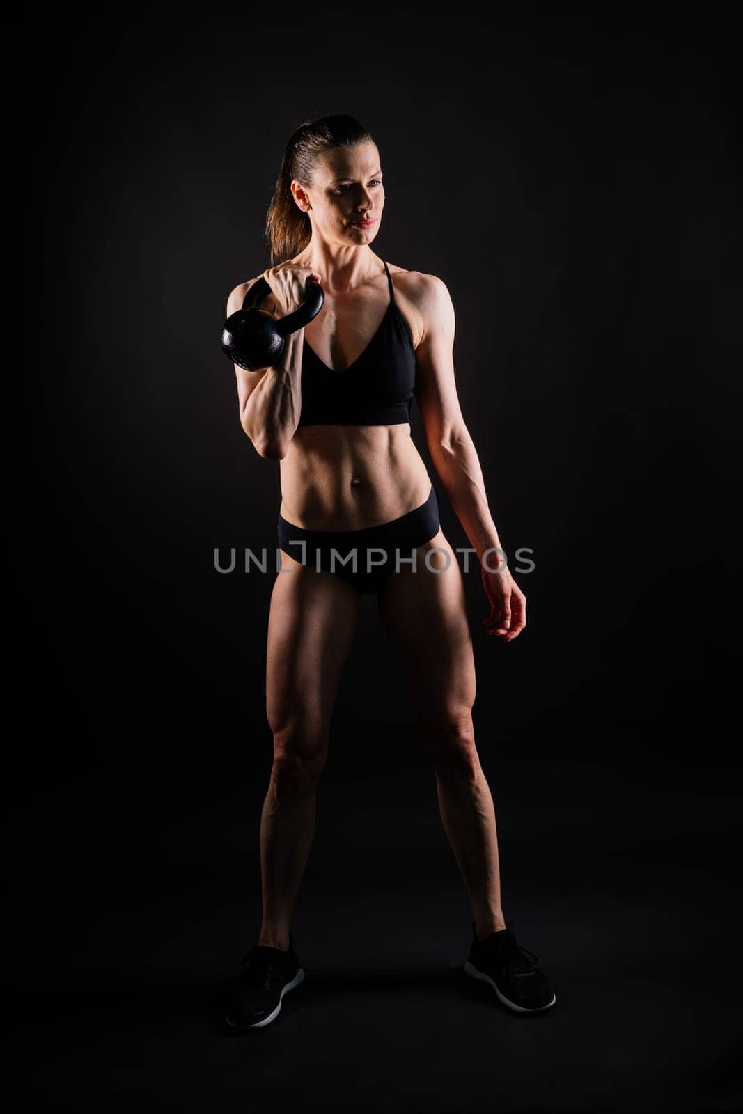 Tough fitness female model with kettle bell on a grey dark yellow red background.