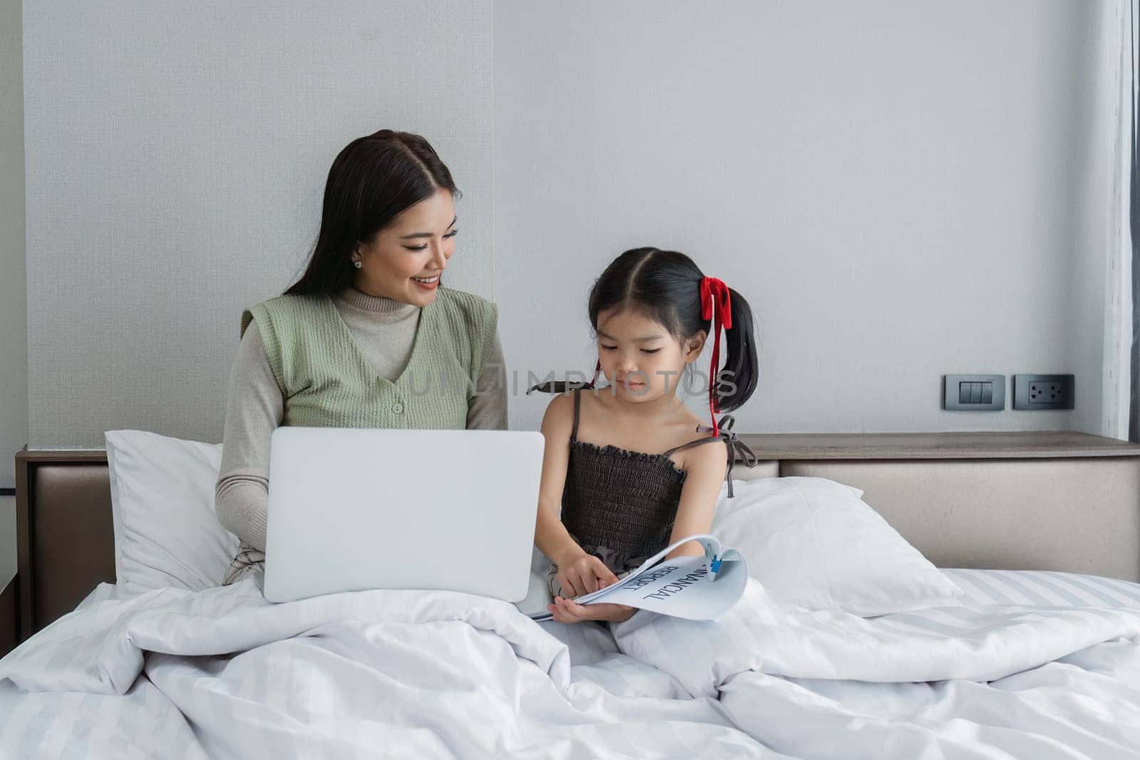 Work from home, freelance and lifestyle concept. Portrait of creative asian female sitting on bed with laptop and her take care of her kid while working by itchaznong