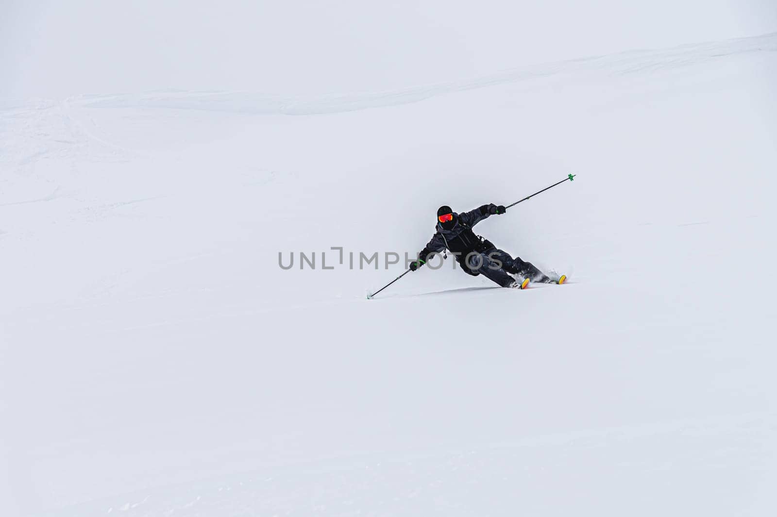 A skier on the piste, going down the slope among the Alpine mountains, which are not visible due to cloudiness.