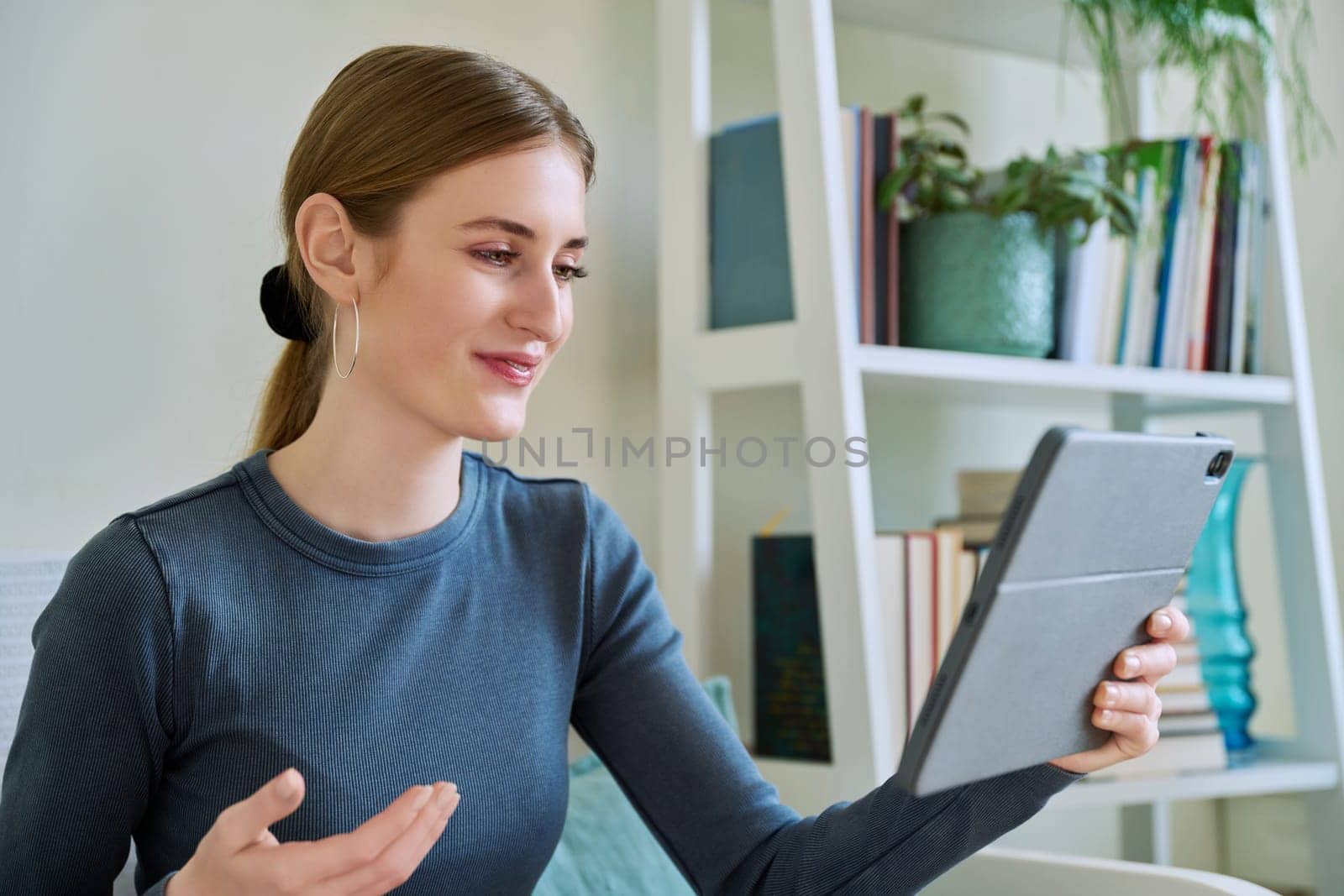 Teenage female student at home looking talking in web camera of digital tablet by VH-studio