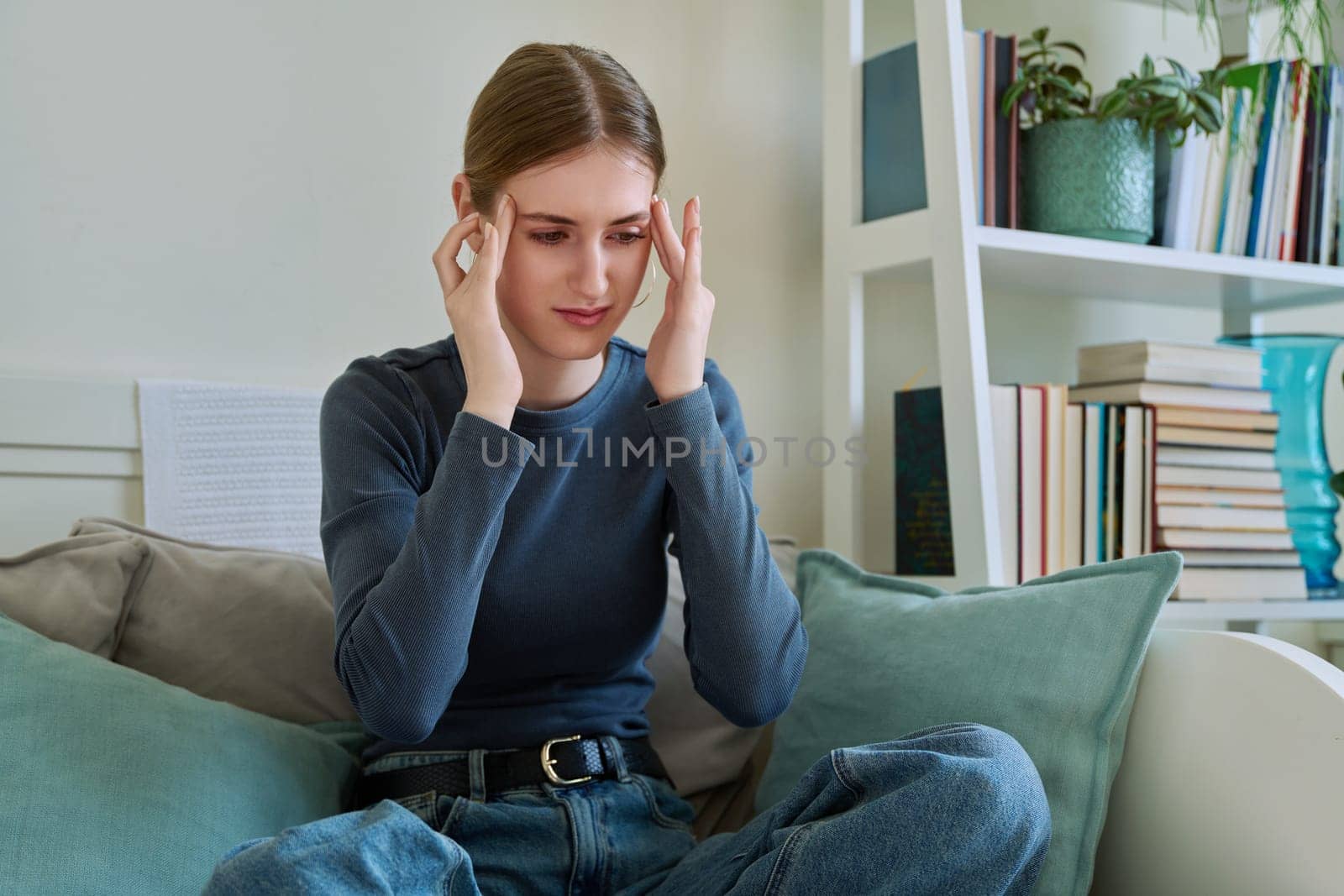 Young suffering teenage female having headache, holding head with hands, sitting on couch at home. Health, problems, mental difficulties, depression, youth concept