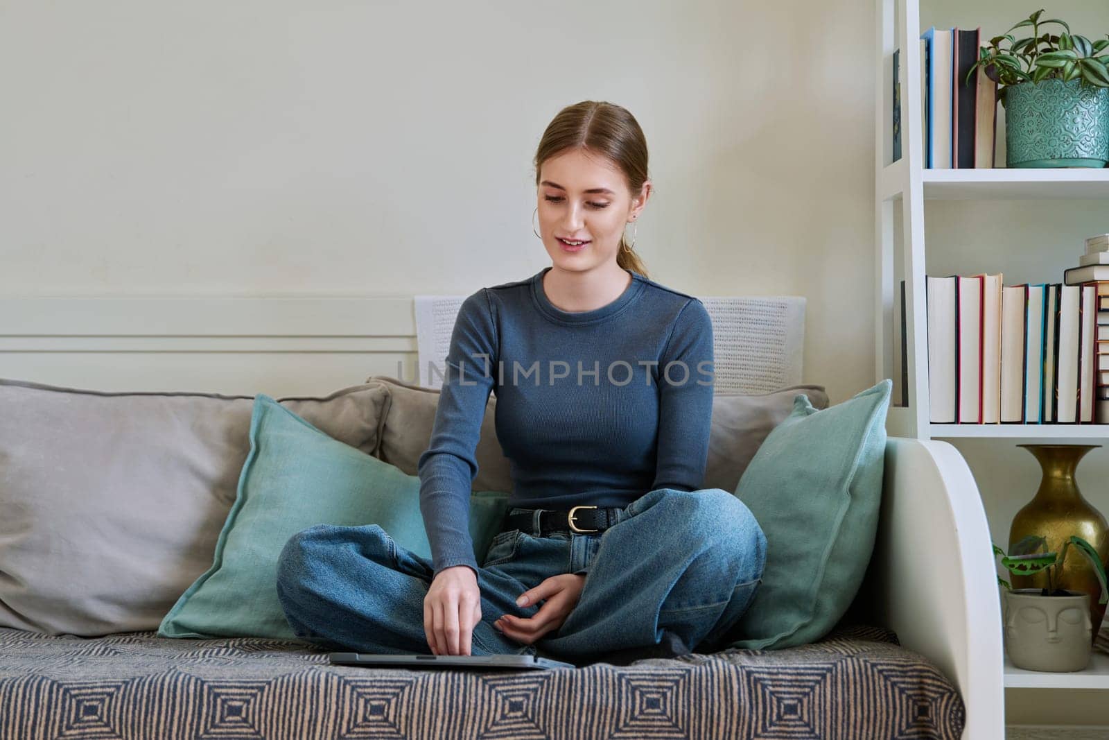 Young female teenager with digital tablet, stylus drawing illustrating sitting on couch at home. Technologies, leisure, creativity, education, freelance work, lifestyle, youth concept