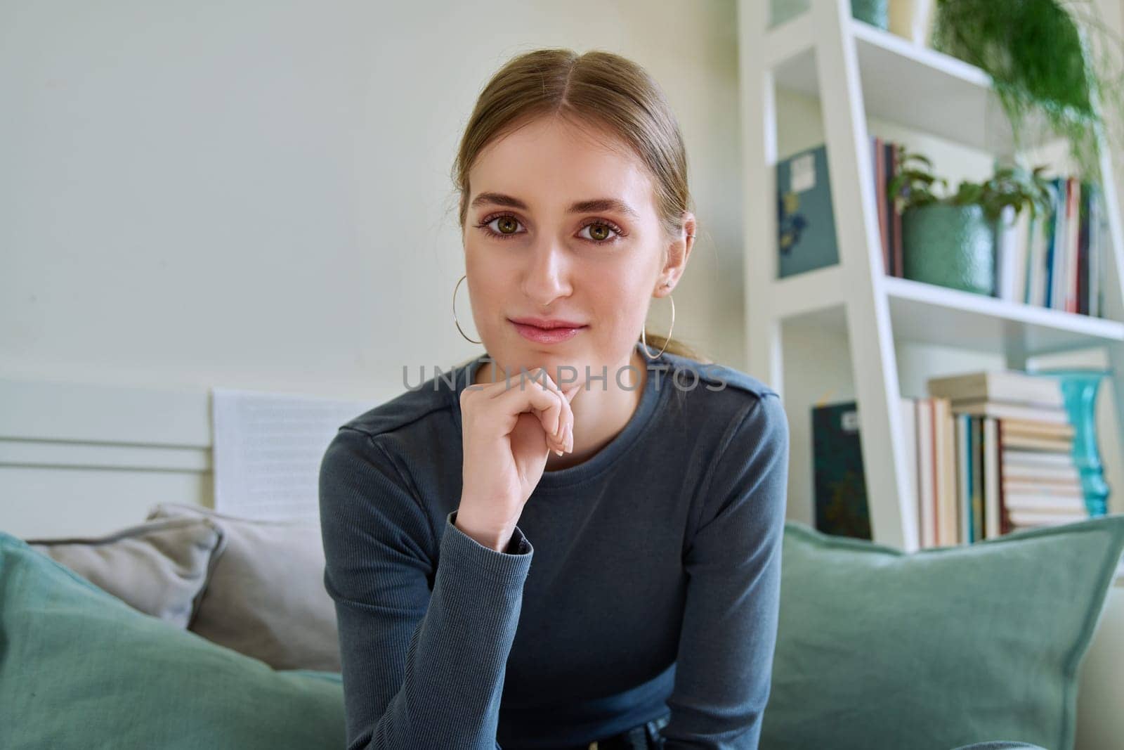 Portrait of beautiful happy smiling teenage girl looking at camera, sitting on couch at home. Age 16,17,18 years, lifestyle, youth concept