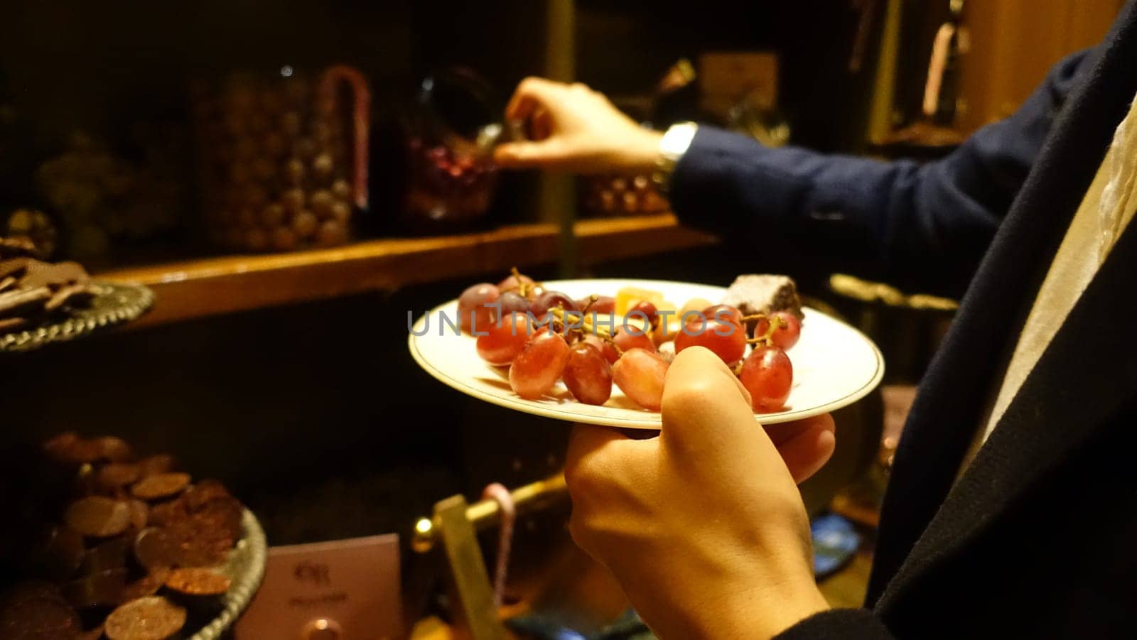 A person is holding a small plate with grapes and a piece of cheese.