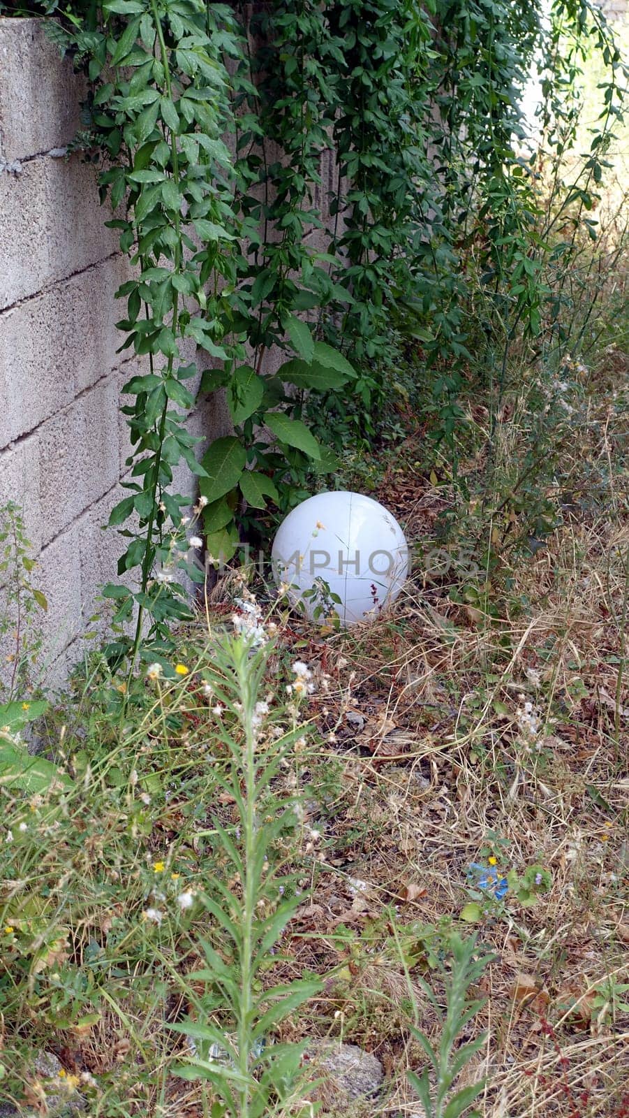 A white crystal sphere lying on the grass next to a wall during a hot summer day.