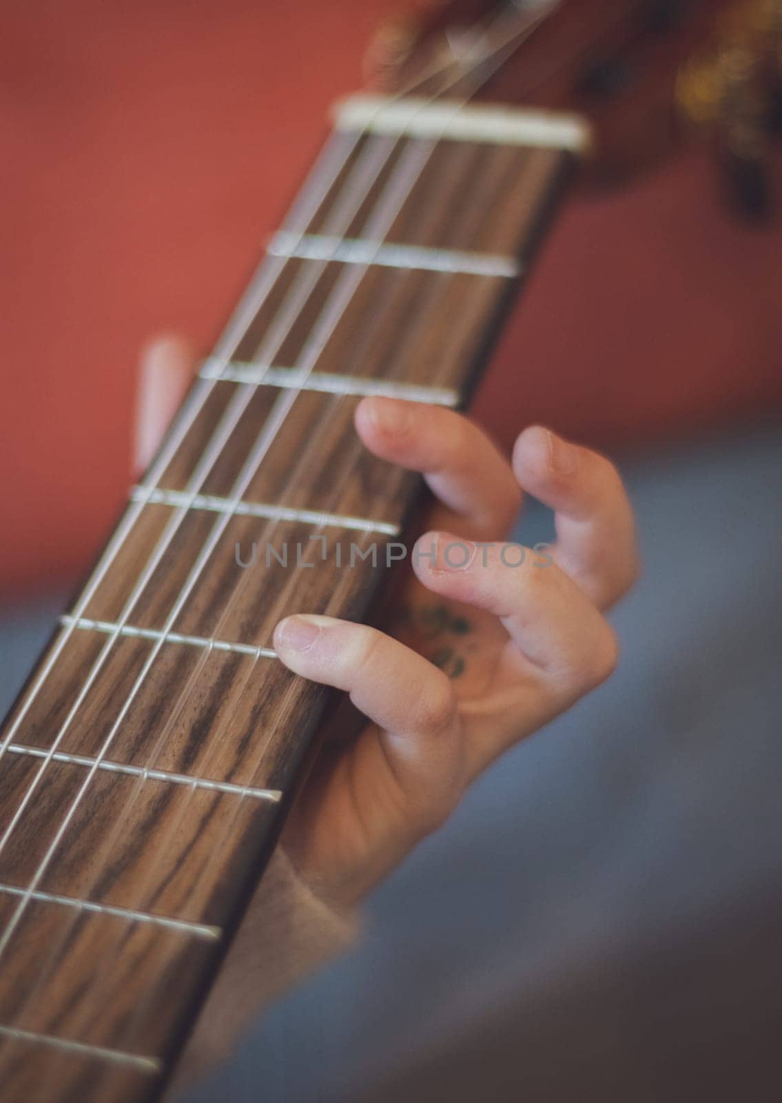 Little caucasian girl holding a guitar and pinching the strings with her fingers, close-up side view. Music education concept.