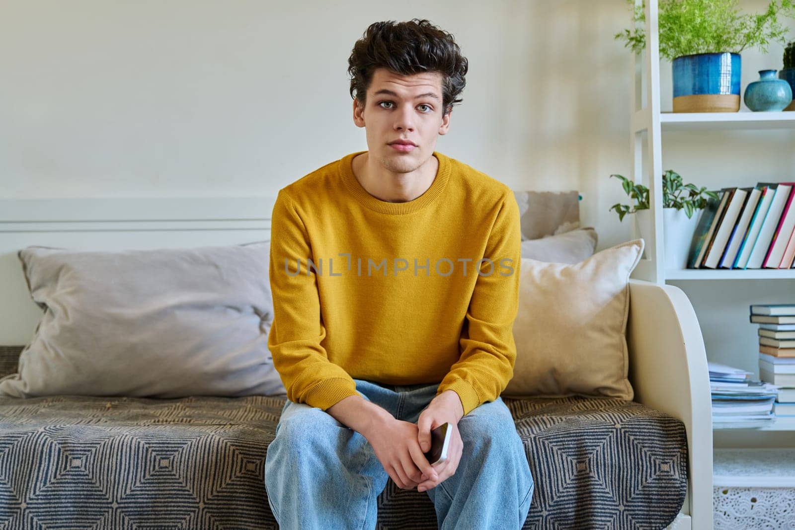 Portrait of handsome guy looking at camera, sitting on couch at home by VH-studio