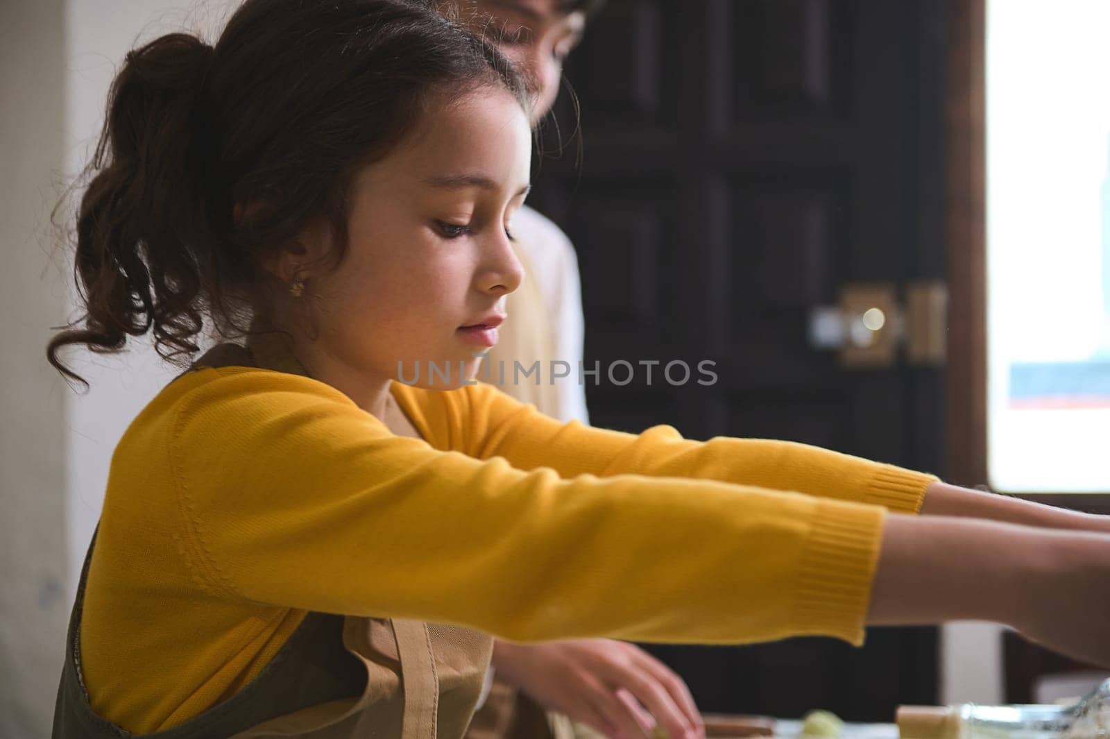 Close-up portrait of a Caucasian little chef girl preparing dumplings during cooking master class indoors. Kids education and development, Food and drink consumerism. People. Happy carefree childhood
