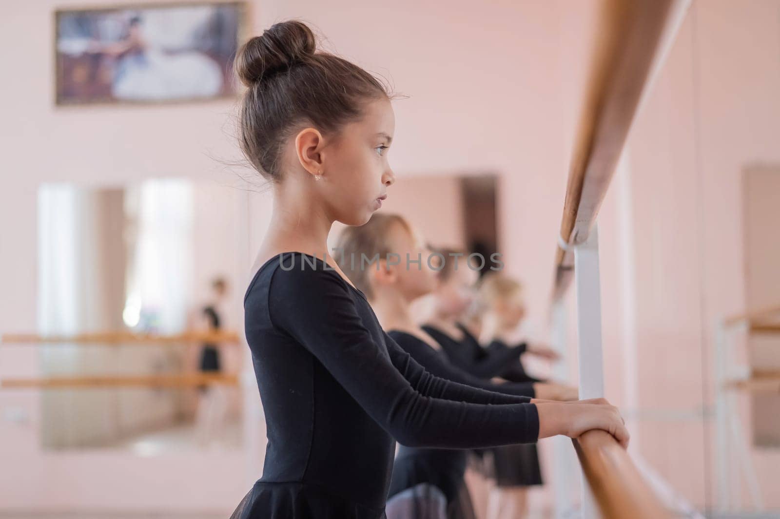 Cute little girls in black swimsuits and tutu do ballet at the barre