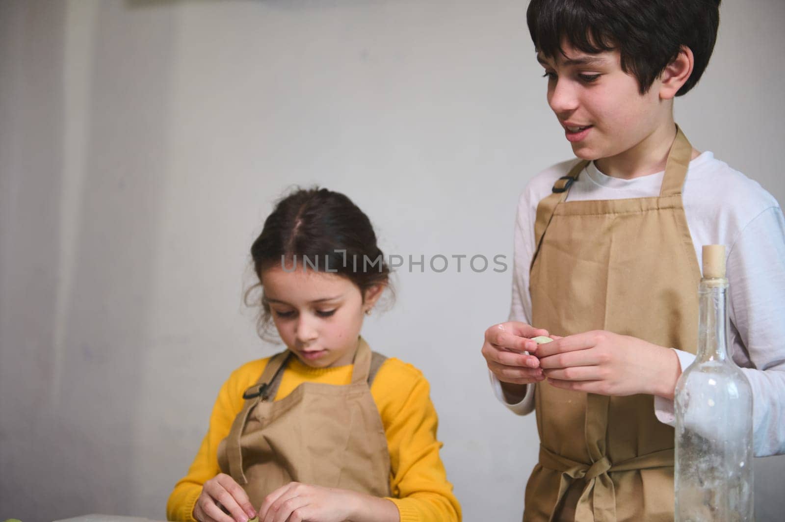 Boy and girl learning culinary at cooking class, making homemade dumplings with mashed potato filling, standing at floured kitchen table with ingredients at rustic kitchen in a rural house