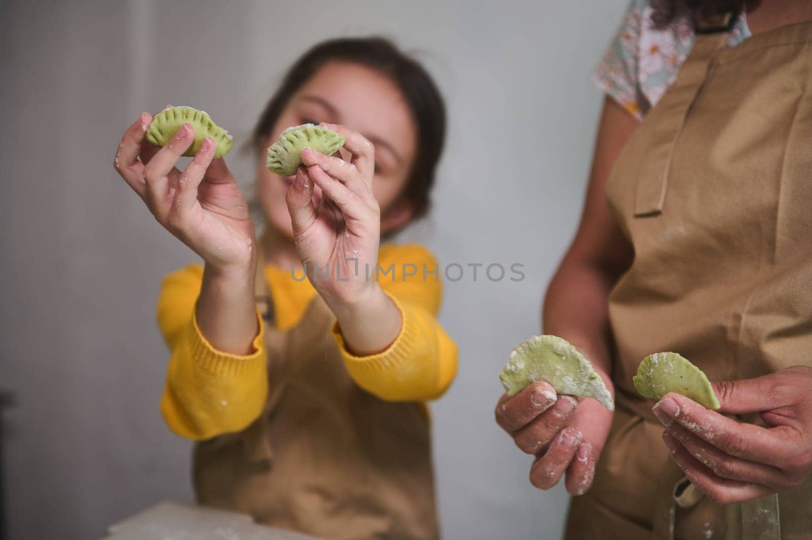 Details on sculpted dumplings in child girl's hands. Kids learning cooking during culinary masterclass. Mother and daughter cooking together traditional homemade Ukrainian varennyky for family dinner