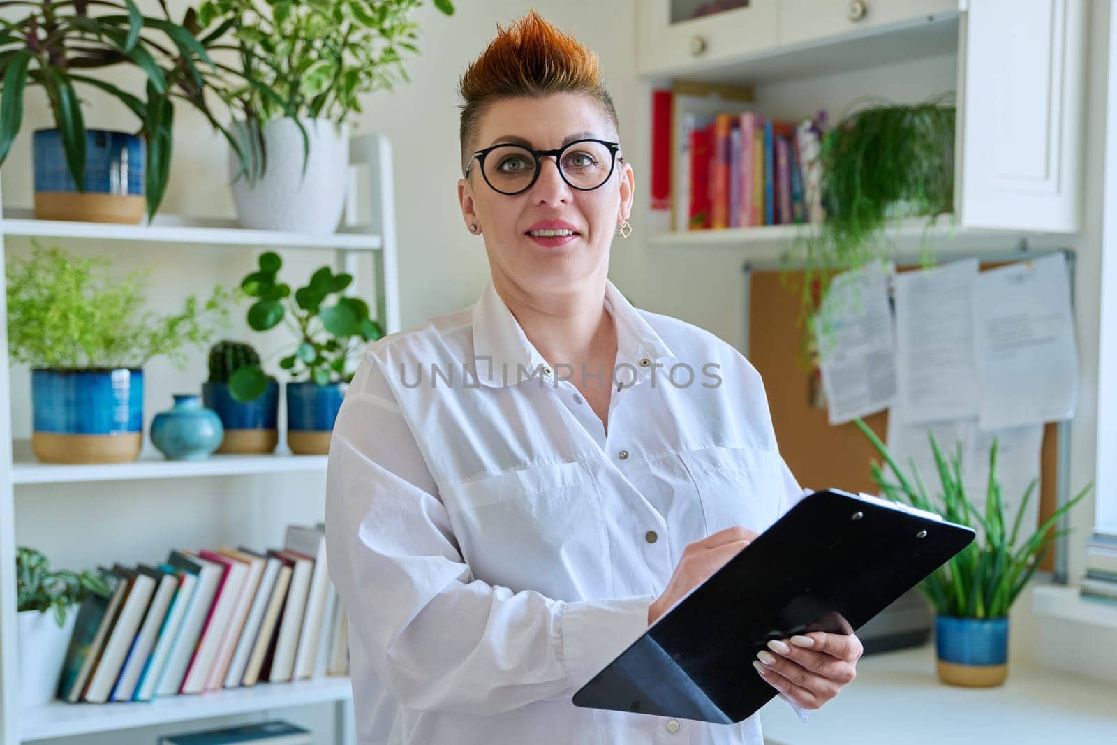 Portrait of smiling female psychotherapist with clipboard at workplace in office. Professional mental therapist counselor psychologist social worker looking at camera. Health care services, treatment