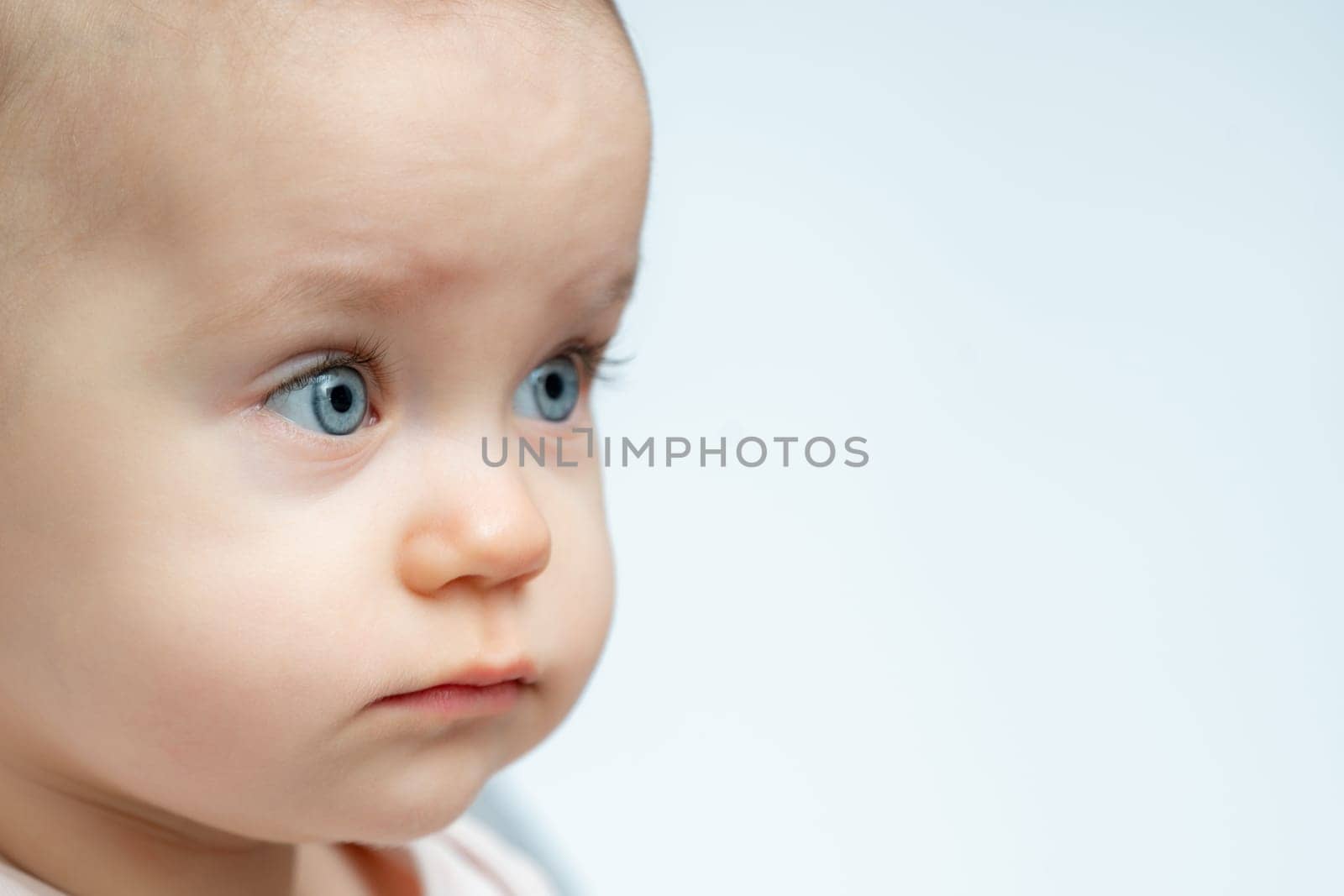 One year old baby gazes to the side with curious eyes. Concept of innocence and wonder in childhood by Mariakray