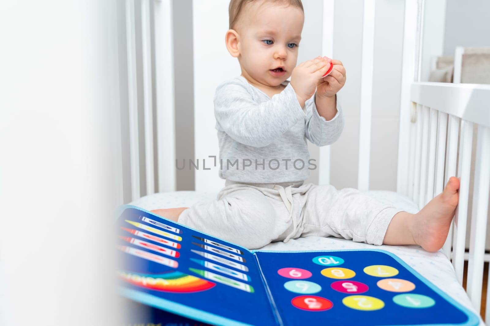 One year old baby sitting in a crib playing with montessori busy book