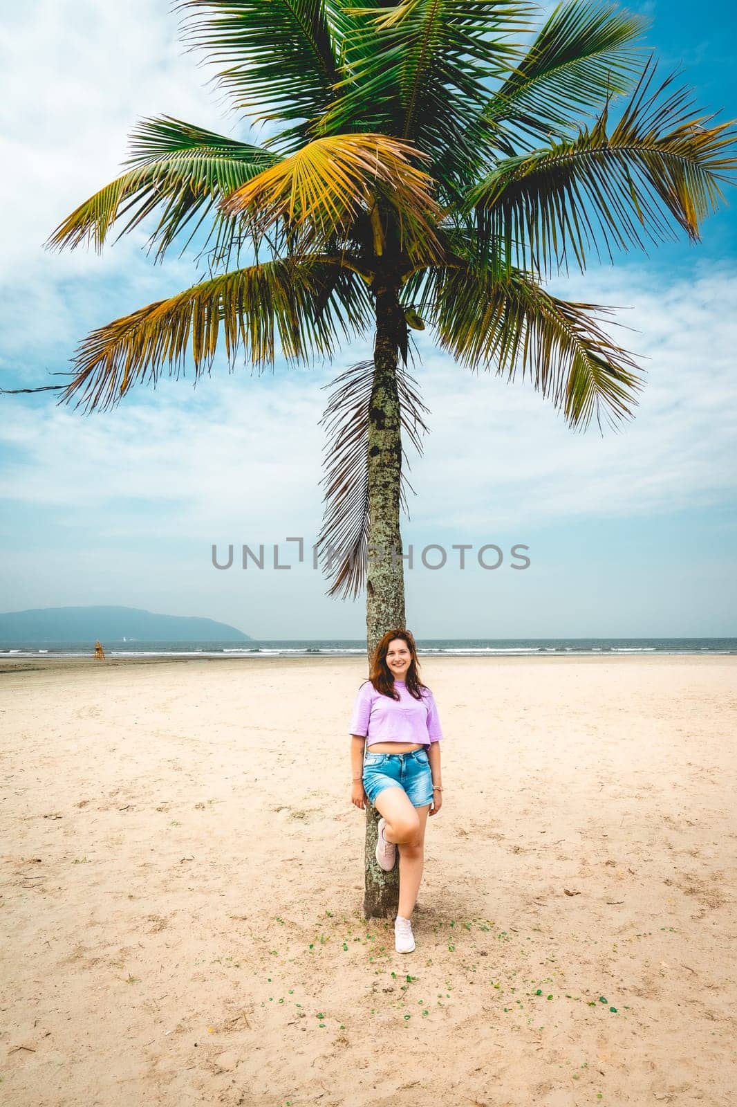 Brazilian Woman posing at a palmtree at the beach of Santos, Brazil.