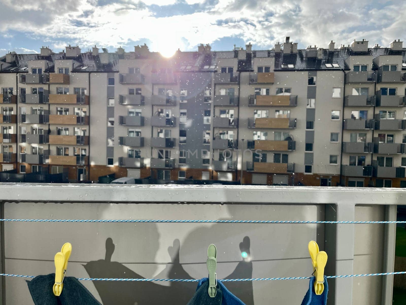 There is a rope with clothespins on the balcony, the bright sun is shining between the houses and the rain is falling. High quality photo