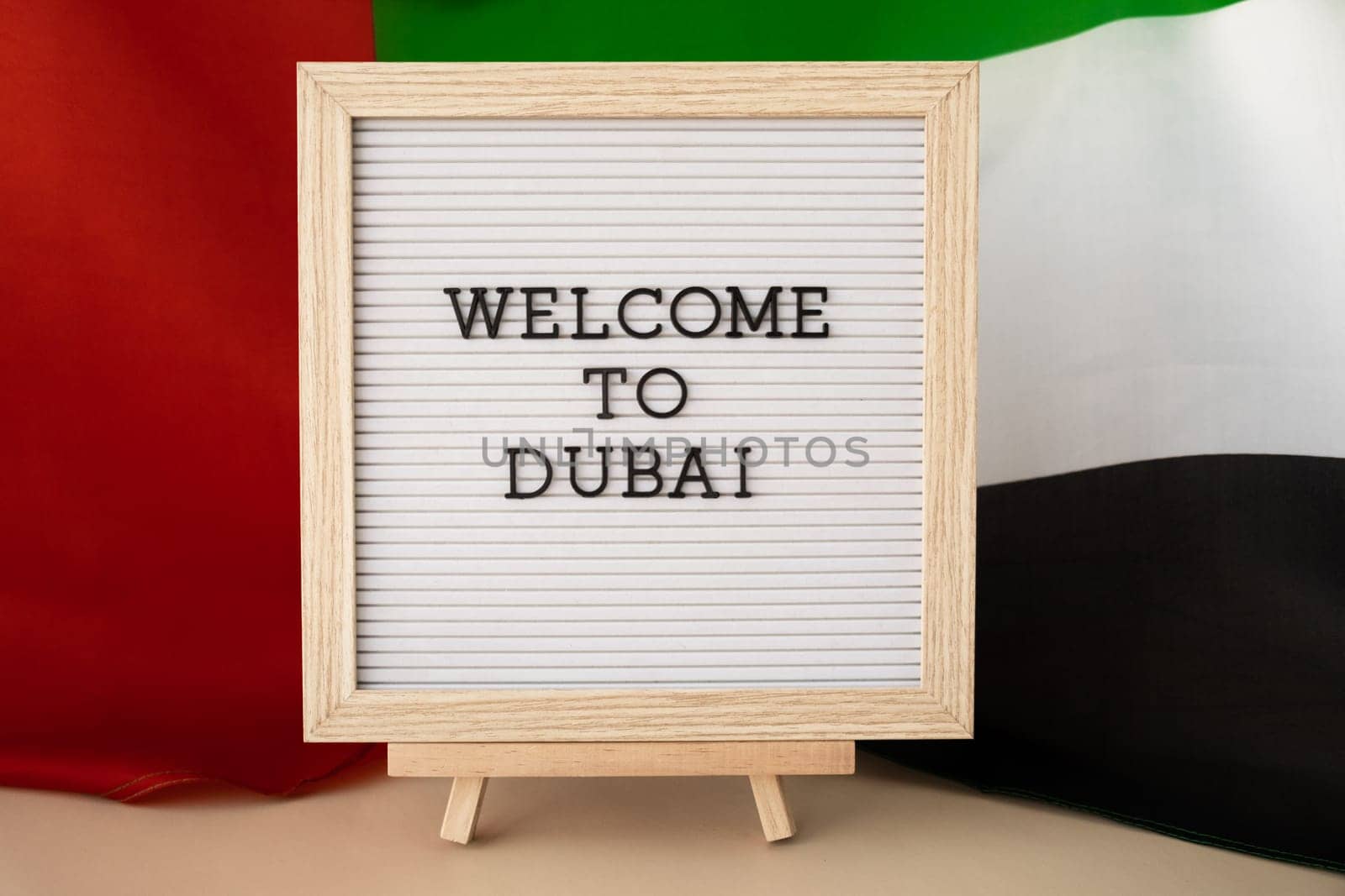 Message text WELCOME TO DUBAI on background of waving UAE flag made from silk. United Arab Emirates flag with concept of tourism and traveling. Inviting greeting card, advertisement. Dubai welcoming card