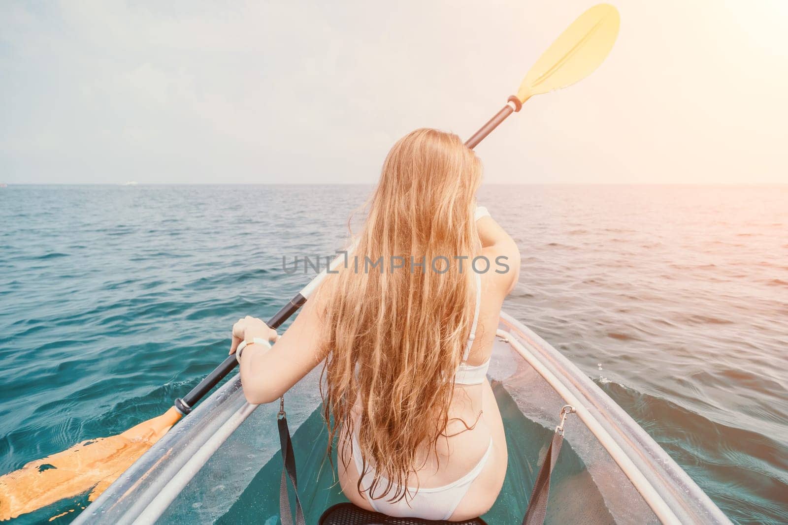 Woman in kayak back view. Happy young woman with long hair floating in transparent kayak on the crystal clear sea. Summer holiday vacation and cheerful female people relaxing having fun on the boat by panophotograph