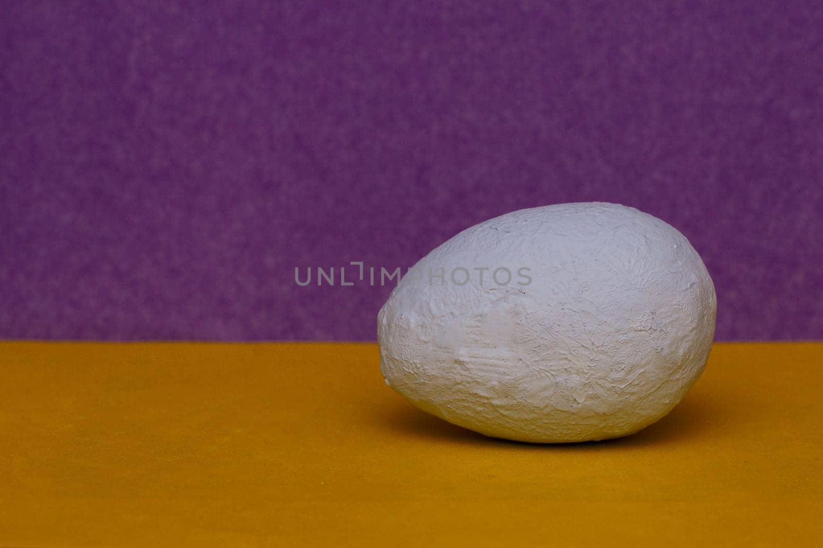 A light blue hand painted decorative egg on a yellow and purple background.copy space