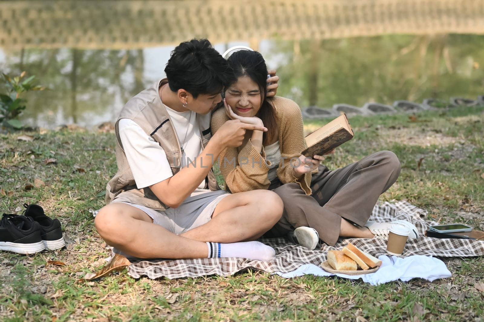 Happy young couple having breakfast sitting together on the picnic blanket in city park by prathanchorruangsak
