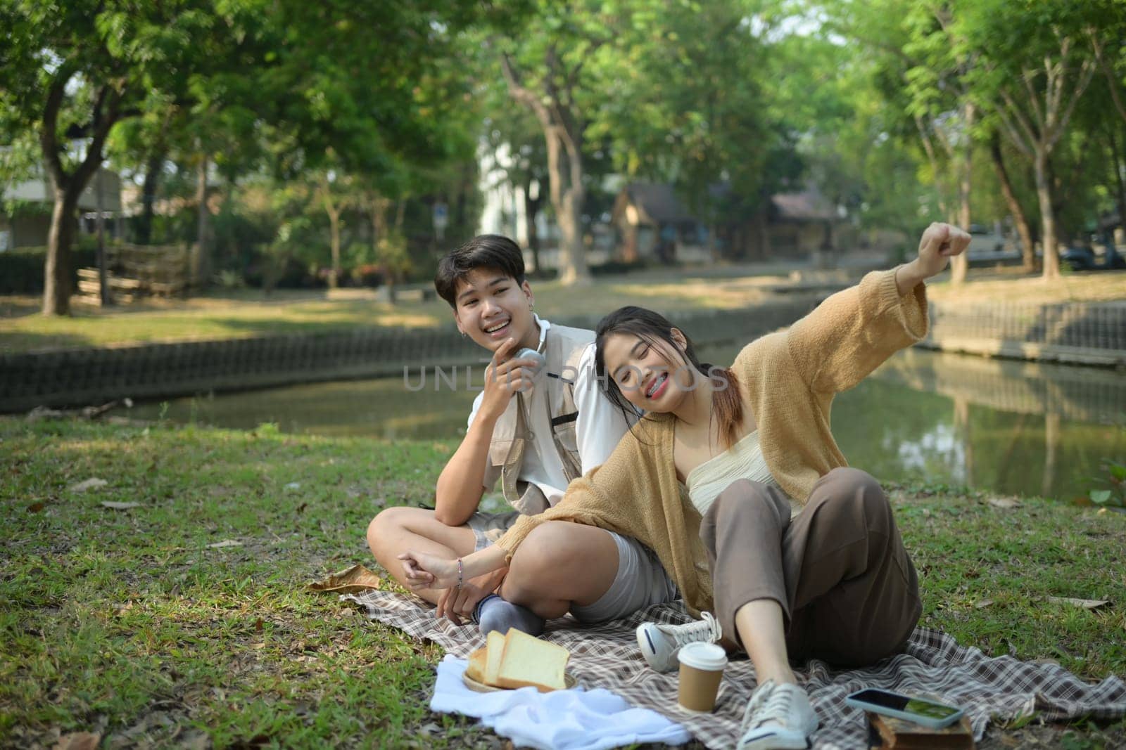 Young beautiful couple laughing, enjoying picnic time on a beautiful sunny day by prathanchorruangsak