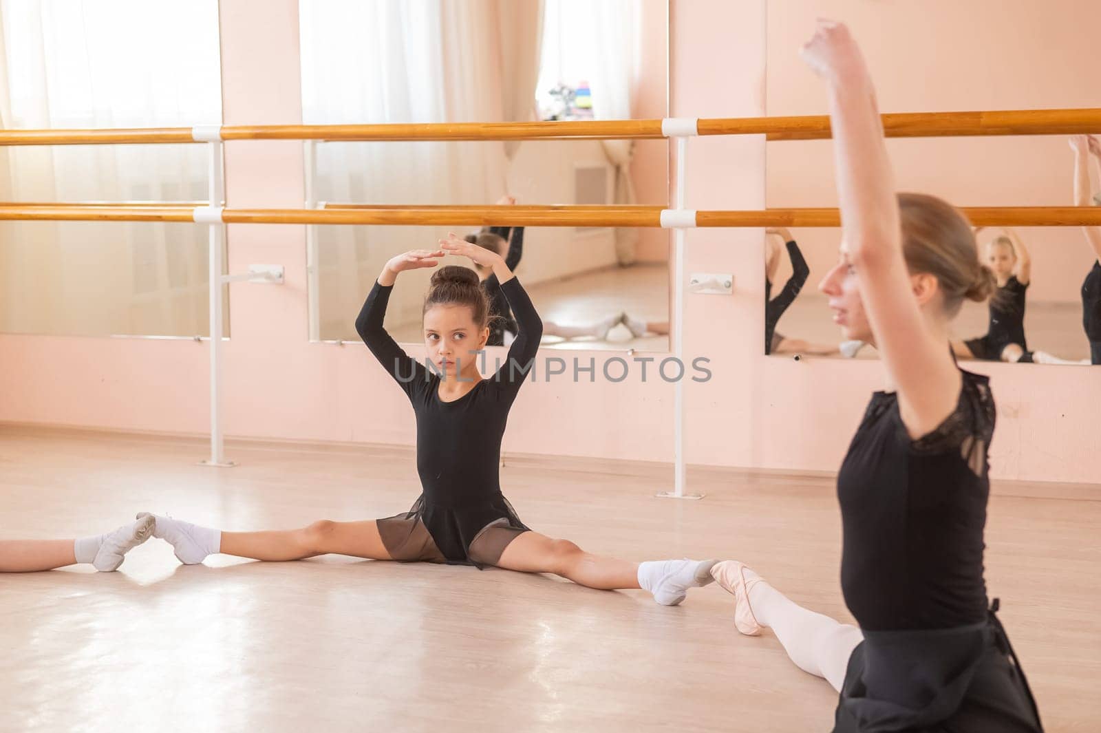 Caucasian woman little girls sit in a circle and do stretching at a ballet school