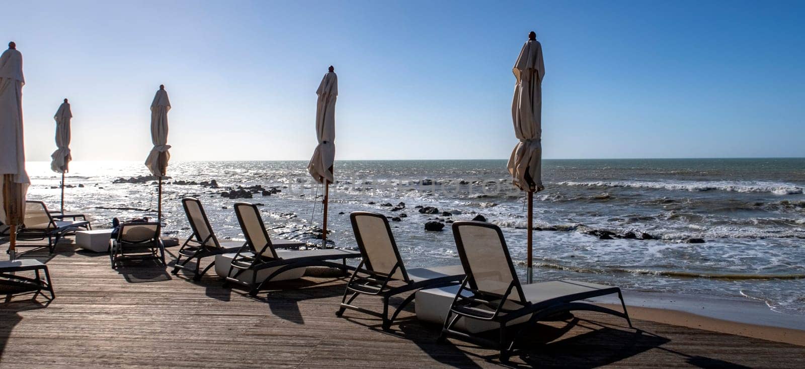 Chaise lounges and umbrellas near the sand on the coast of the azure sea and against the blue sky,	