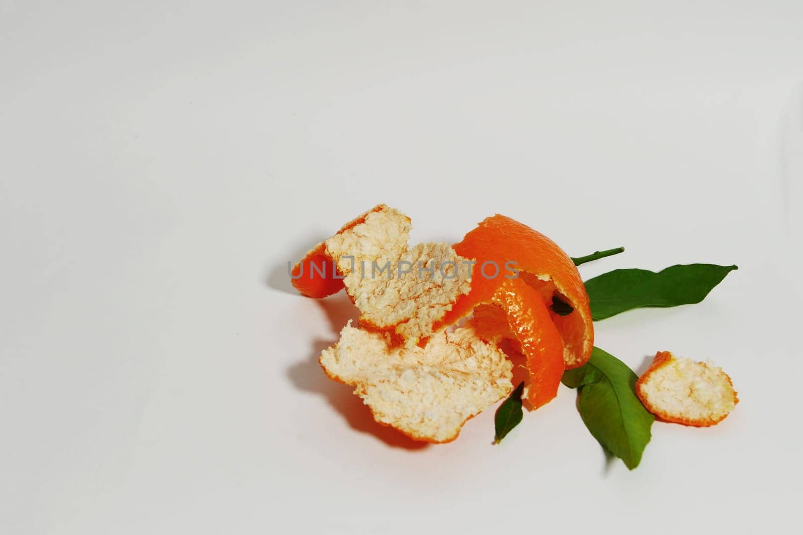 Peel of ripe tangerine and green leaves on a white paper background.