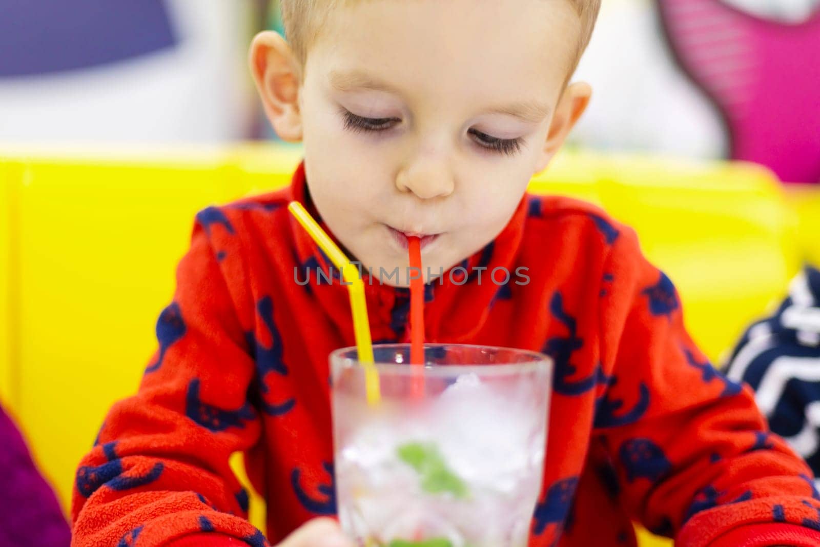Little boy sipping water with mint leaves through a straw from a clear glass by andreyz