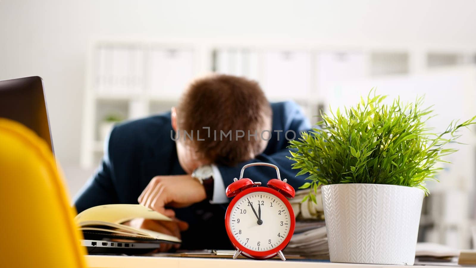 Red alarm clock shows late time closeup and tired office male clerk in suit take nap on table workplace full of exam papers. Career frustration freelance employment fail study problem low energy down