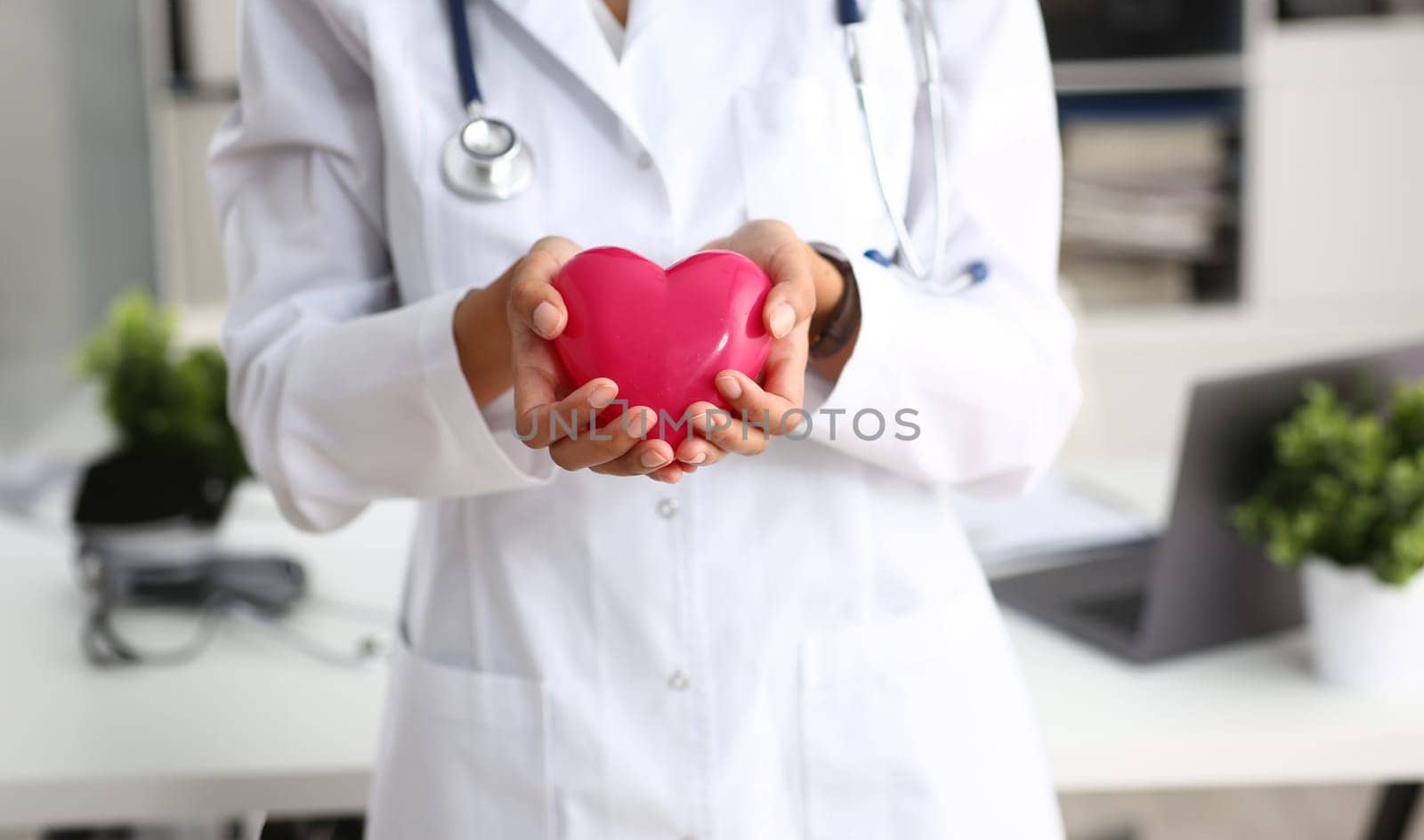Female doctor hold in arms and cover red toy heart closeup. Cardio therapeutist student education CPR 911 life save physician make cardiac physical pulse rate measure arrhythmia lifestyle