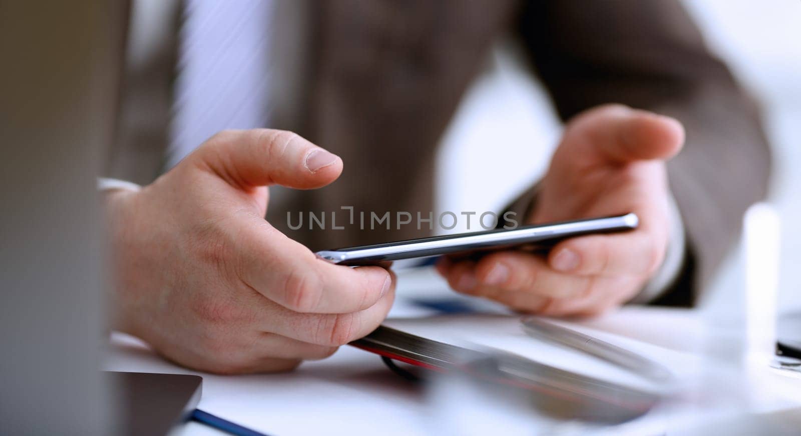 Male arm in suit hold phone and silver pen at workplace closeup. Read news mania send sms chat addict use electronic bank modern lifestyle job plan colleague share blog tweet web application search