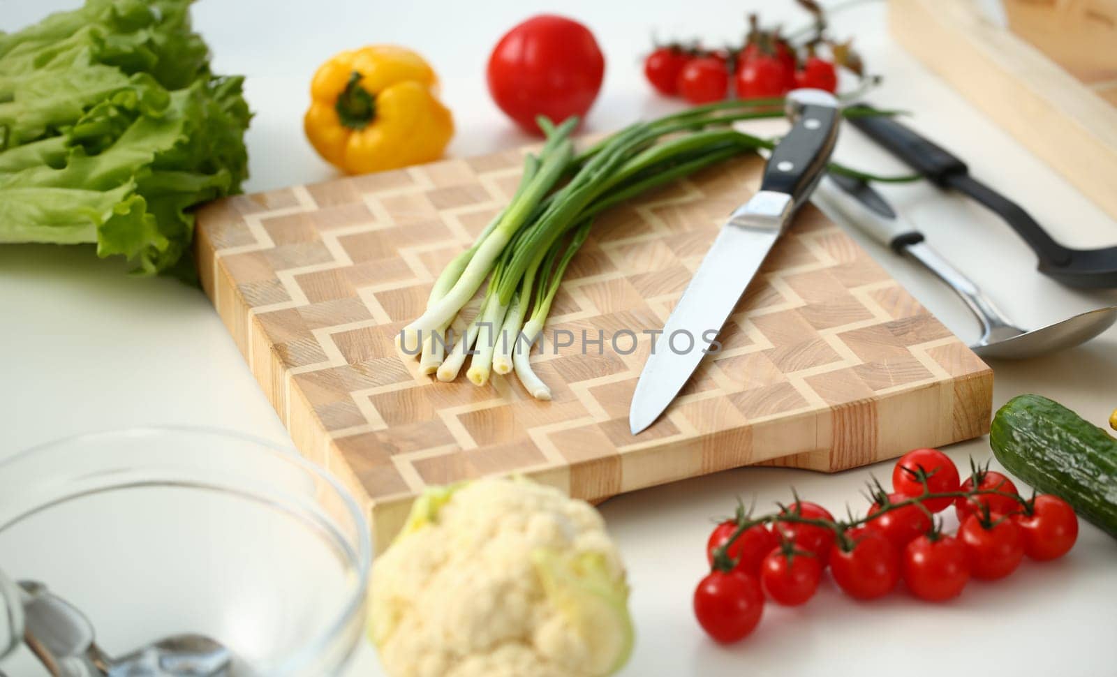Knife and green onions for salad or fresh vegetable soup with vitamins are on wooden cutting board. Raw food and vegetarian food recipe book in modern society is a popular concept.