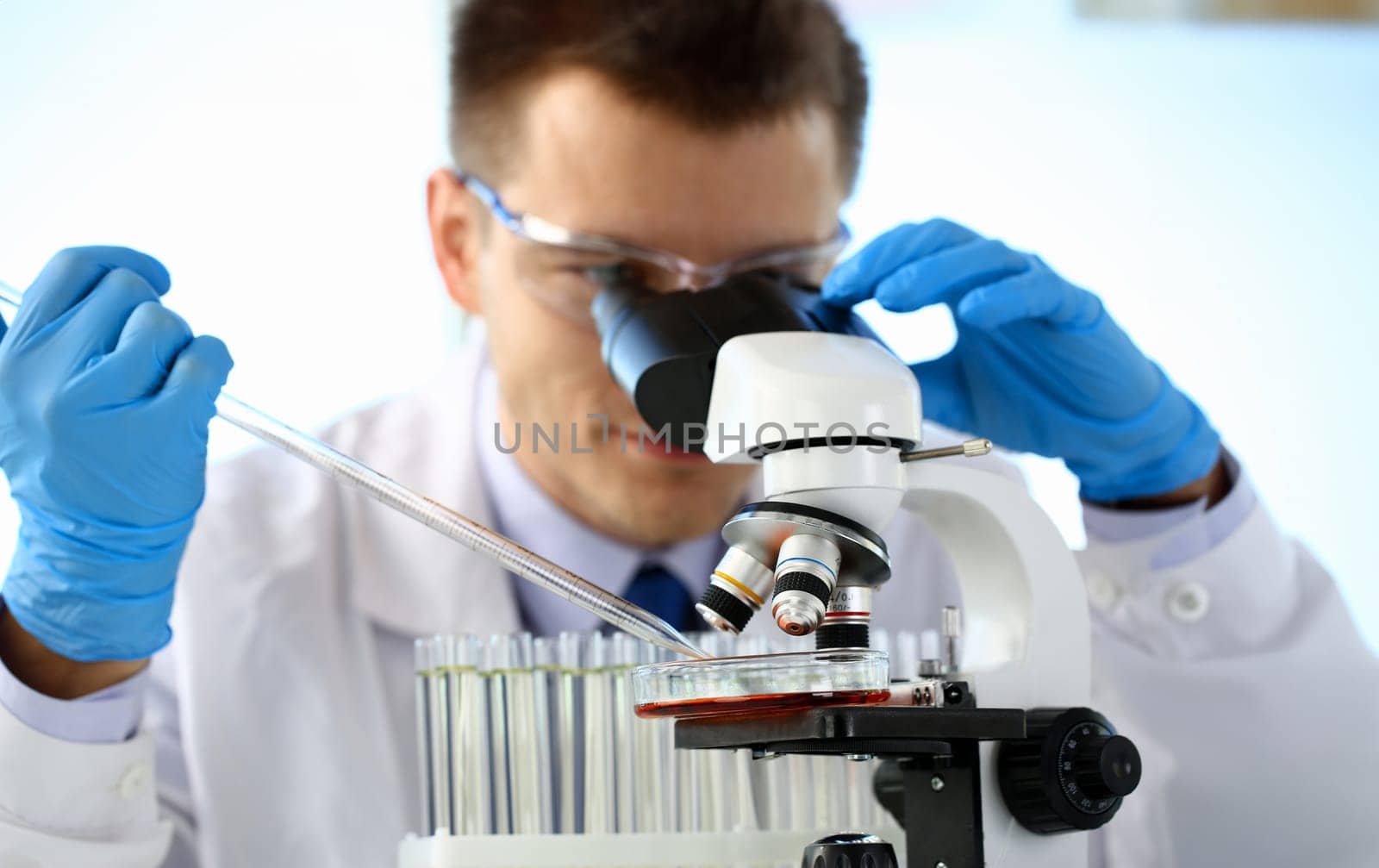 Portrait of a young chemist looking in binocular microscope looking for pathology analyzes patient at medical hospital for treatment disease tumors