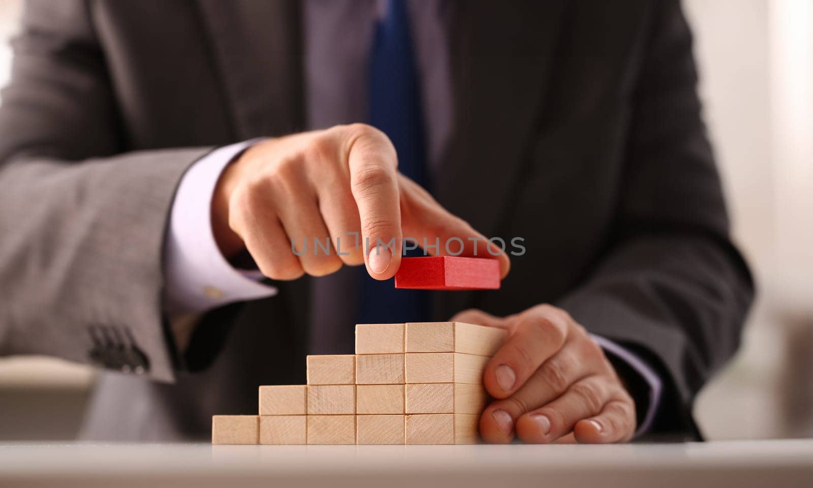 Male hand holds red wood block of stair finish next step rare progress personnel talent authority hot pyramid background on ladder different insurance concept closeup