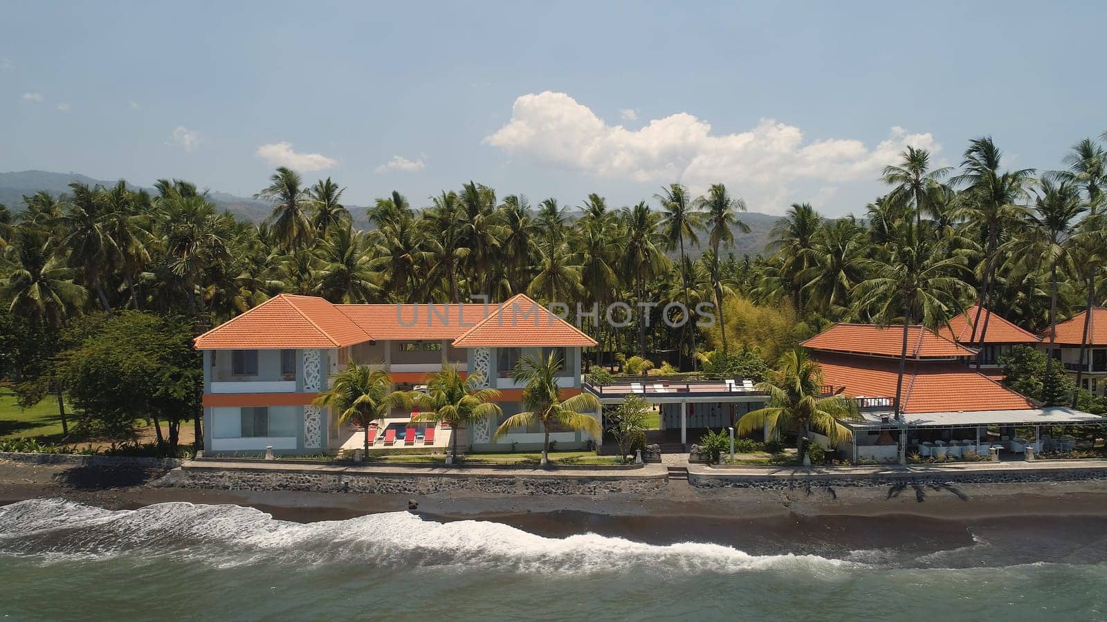 aerial view luxury hotel with swimming pool, sun beds, palm trees by sea. seascape coastline with black sand beach, palm trees, hotel, tropical resort. Bali,Indonesia, travel concept.