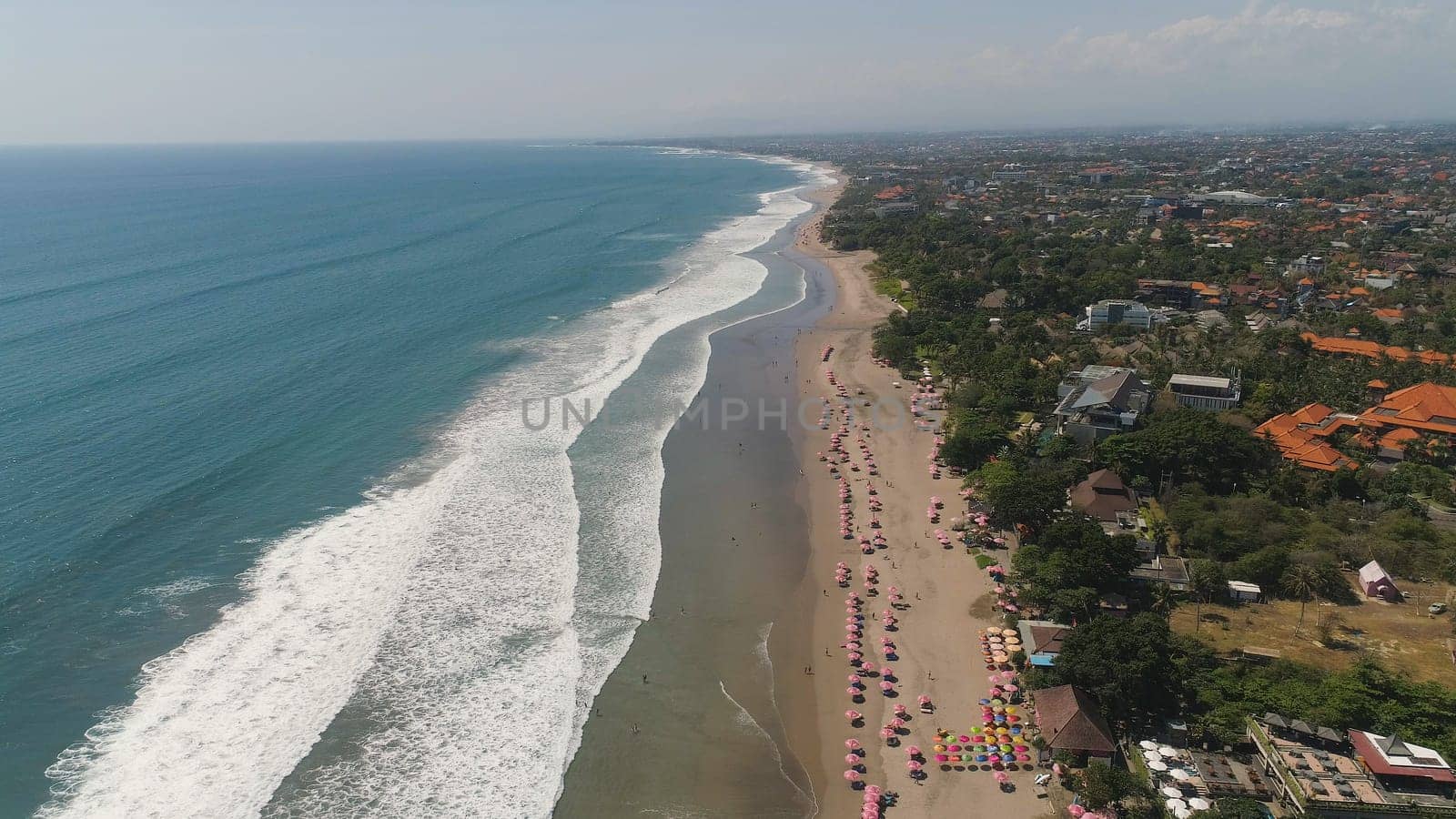 Aerial view sand beach with resting people, hotels and tourists, sun umbrellas, Bali, Kuta. surfers on water surface. Seascape, beach, ocean, sky sea Travel concept