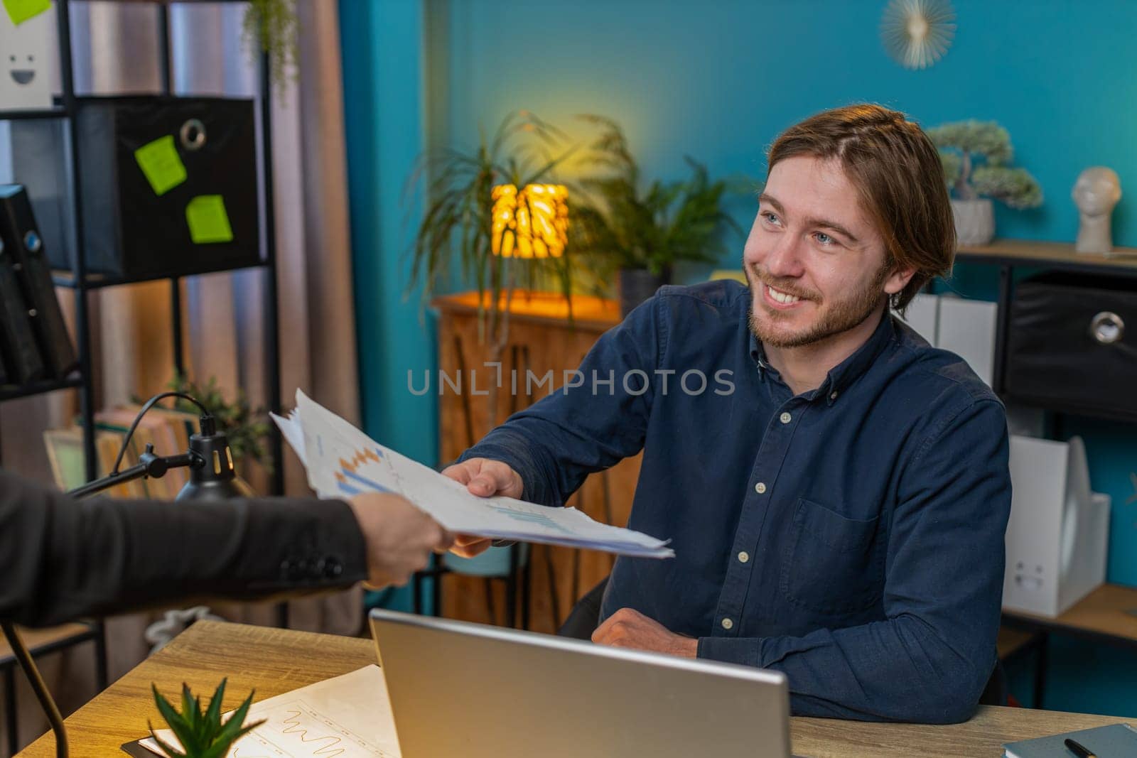 Caucasian freelancer businessman receiving documents from boss and working with financial graph, calculate taxes for charts and reports in home office. Guy working on laptop, planning expenses budget.