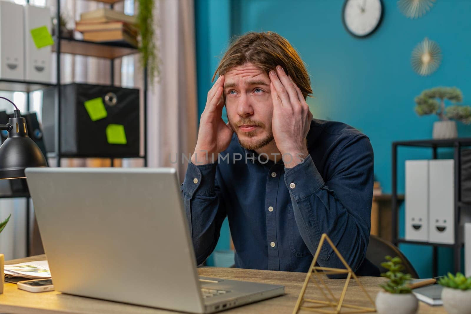 Tired ill Caucasian businessman suffering from headache problem tension and migraine, stress at home office table workplace. Bearded freelancer broker worker man works on laptop notebook. Overworking