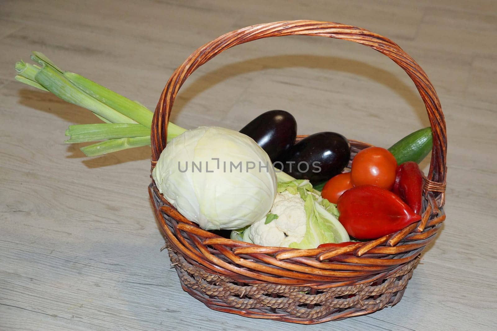 Wicker basket with fresh vegetables, cabbage, cauliflower, peppers, leeks, tomatoes, cucumber eggplants in a basket