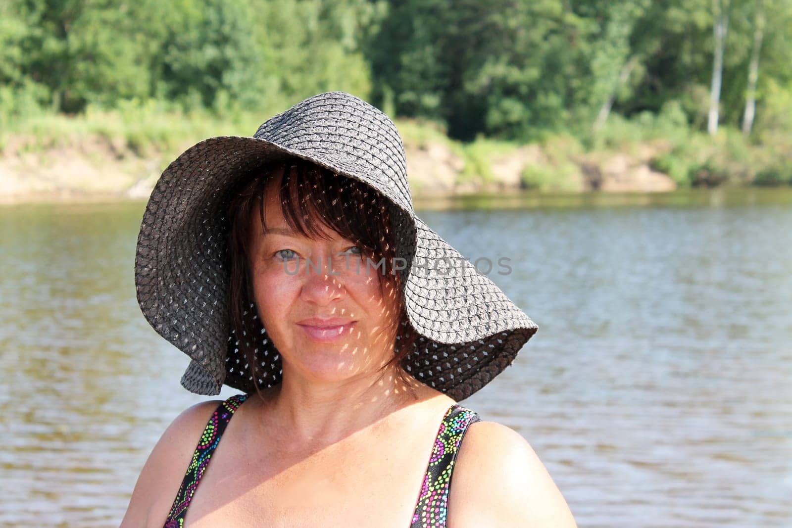 portrait of a smiling middle-aged brunette woman in a straw hat on the river bank on a sunny day.