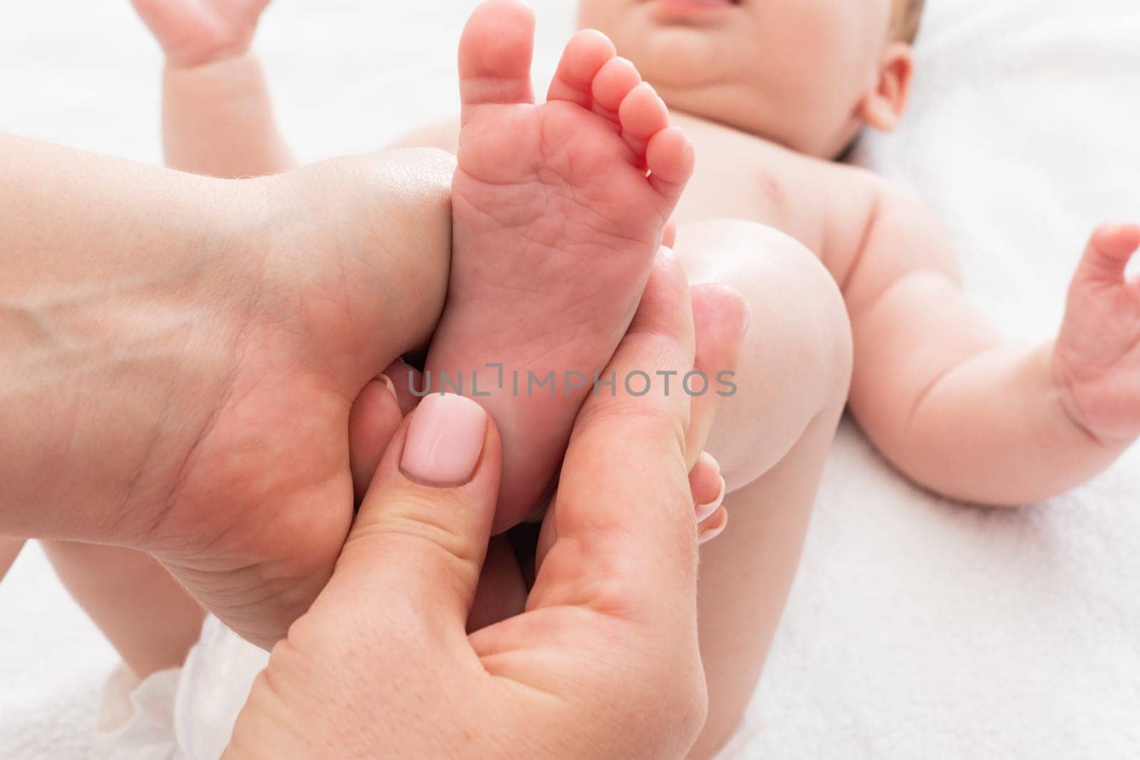 Mother's hands work on infant's feet, Concept of early baby massage benefits by Mariakray